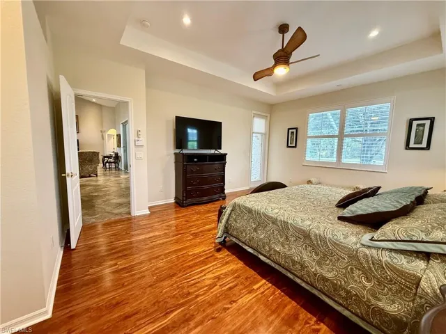 Bedroom with ceiling fan, a tray ceiling, and light wood-type flooring