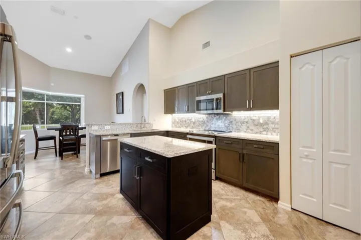 Kitchen featuring light tile flooring, kitchen peninsula, light stone countertops, high vaulted ceiling, and appliances with stainless steel finishes