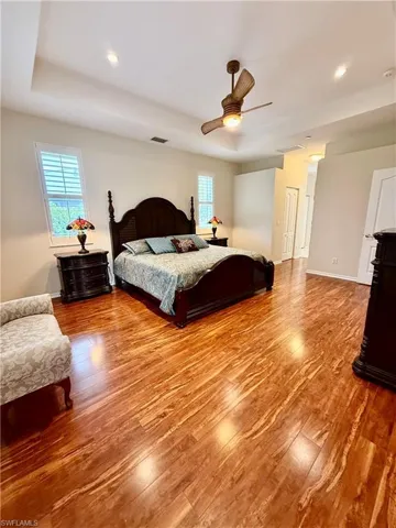 Bedroom with light wood-type flooring, a tray ceiling, and ceiling fan