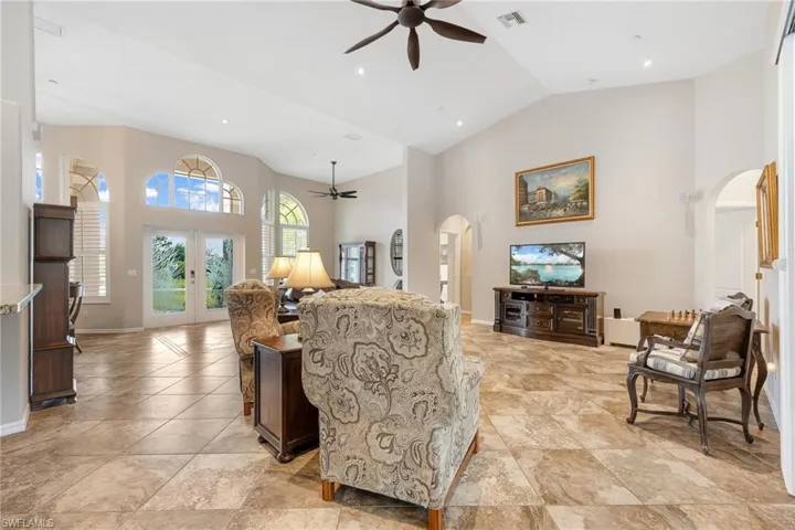 Tiled living room with high vaulted ceiling, ceiling fan, and french doors