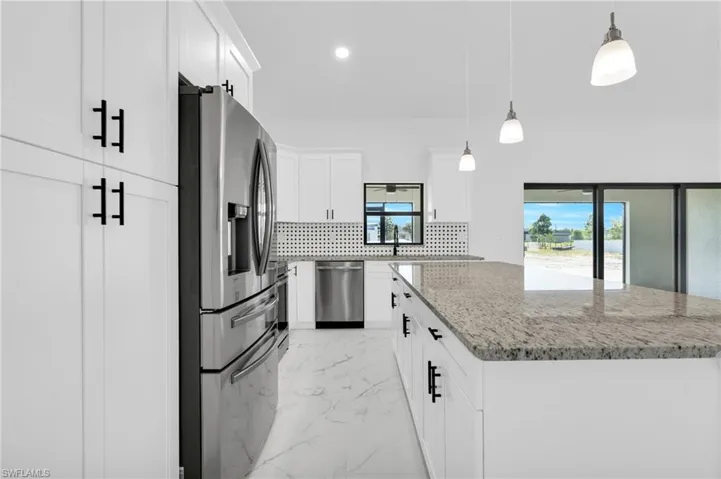 Kitchen featuring light marble finish flooring, appliances with stainless steel finishes, hanging light fixtures, light stone counters, and a kitchen island