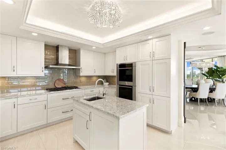 Another view of Kitchen featuring a raised ceiling, an island with sink, white cabinetry
