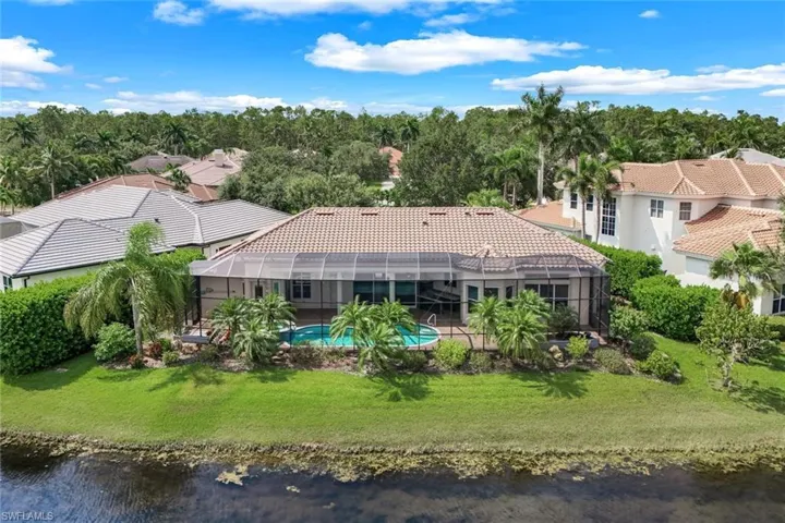 Back of property with glass enclosure, a lawn, and a water view.