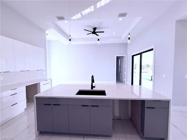 Kitchen with a large island, sink, ceiling fan, a raised ceiling, and pendant lighting