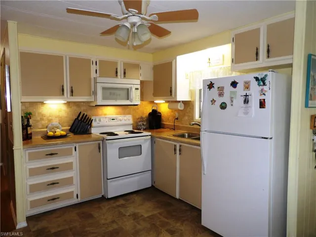 Kitchen with sink, white appliances, ceiling fan, backsplash, and white cabinets