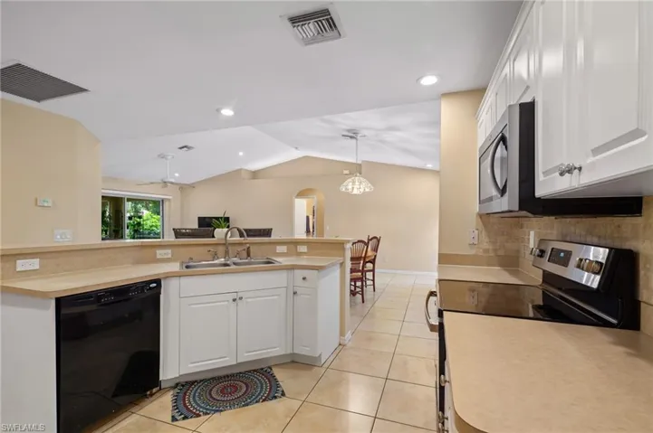 Kitchen with appliances with stainless steel finishes, lofted ceiling, backsplash, light tile patterned floors, and white cabinets