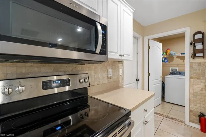 Kitchen with appliances with stainless steel finishes, washer / dryer, white cabinetry, and light countertops