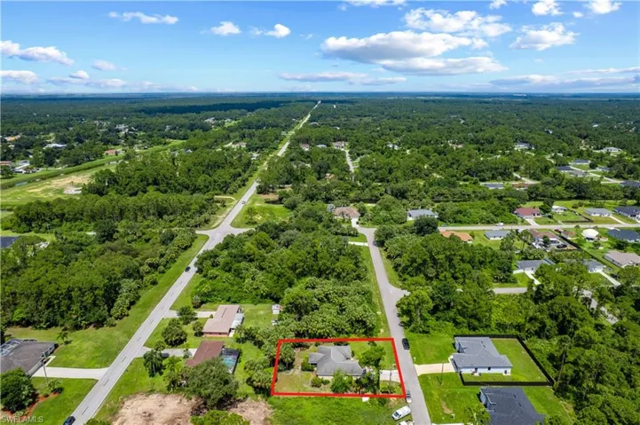 Aerial view of property and surrounding area featuring property parcel outlined and a heavily wooded area
