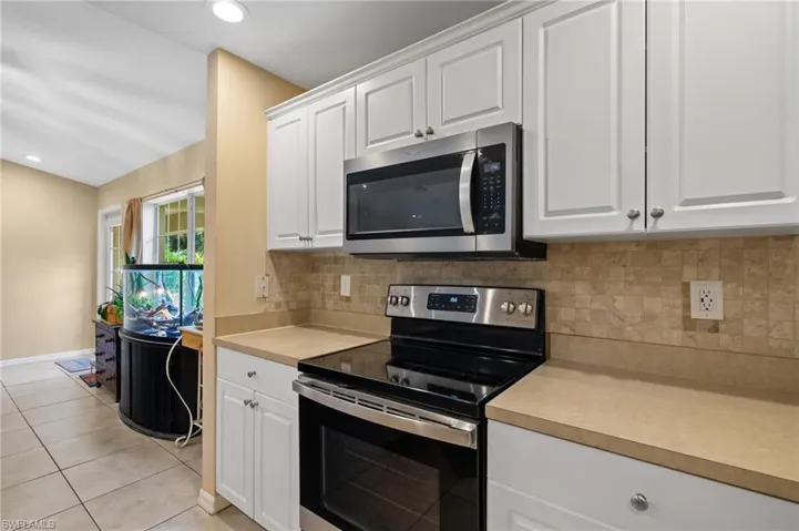 Kitchen with appliances with stainless steel finishes, light countertops, light tile patterned flooring, white cabinetry, and recessed lighting