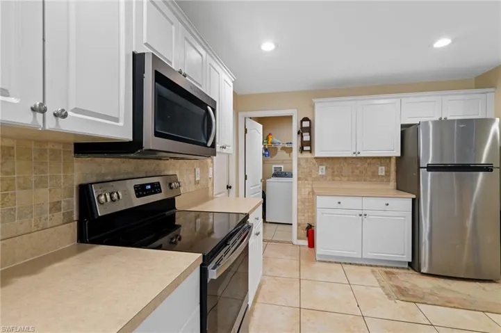 Kitchen featuring appliances with stainless steel finishes, washer / clothes dryer, backsplash, white cabinetry, and light countertops