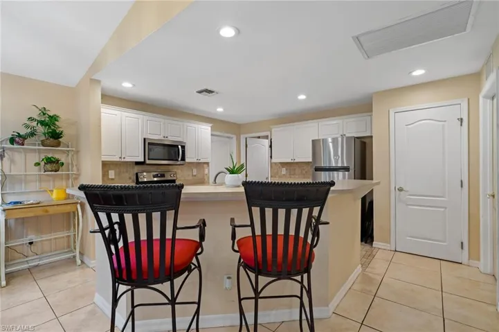 Kitchen featuring appliances with stainless steel finishes, white cabinetry, backsplash, a kitchen bar, and light tile patterned floors
