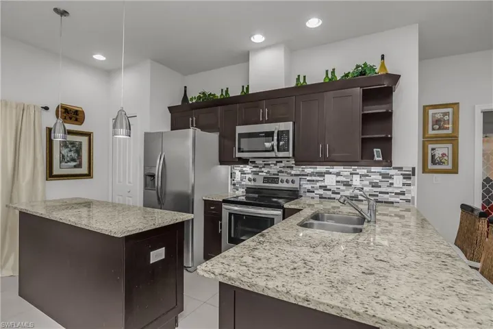 Kitchen featuring dark wood finish cabinets, stainless steel appliances, light stone countertops, open shelves, and a kitchen island