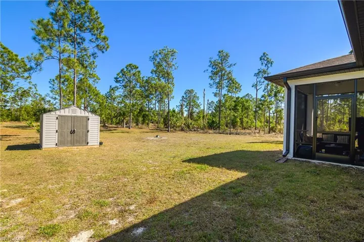 View of grassy yard with a storage unit and a sunroom