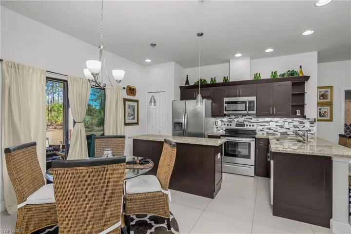 Kitchen with stainless steel appliances, dark wood finish cabinetry, a kitchen bar, light stone counters, and a peninsula
