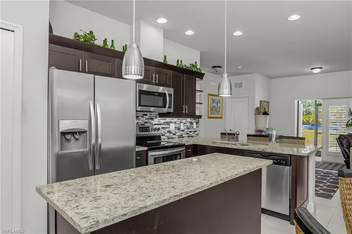 Kitchen featuring dark wood finish cabinets, stainless steel appliances, a peninsula, light stone countertops, and pendant lighting