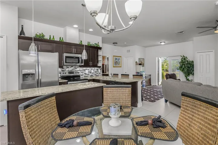Kitchen featuring dark wood finish cabinetry, stainless steel appliances, light stone counters, a chandelier, and a kitchen island