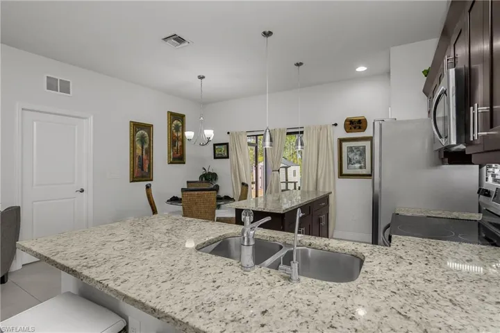 Kitchen featuring stainless steel appliances, dark wood finish cabinets, light stone countertops, a peninsula, and a breakfast bar area