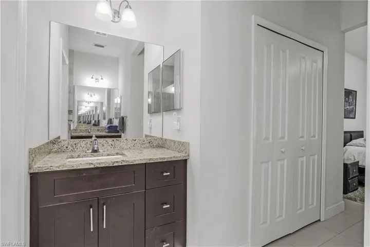 Ensuite bathroom with a closet, vanity, and light tile patterned floors