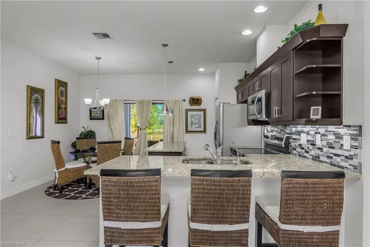 Kitchen featuring a kitchen breakfast bar, a peninsula, light stone counters, dark wood finish cabinetry, and stainless steel appliances