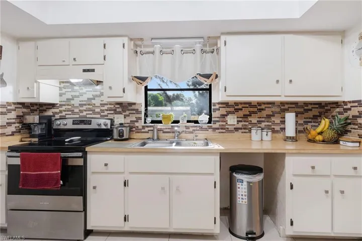 Kitchen with electric stove, sink, light tile patterned floors, decorative backsplash, and white cabinetry