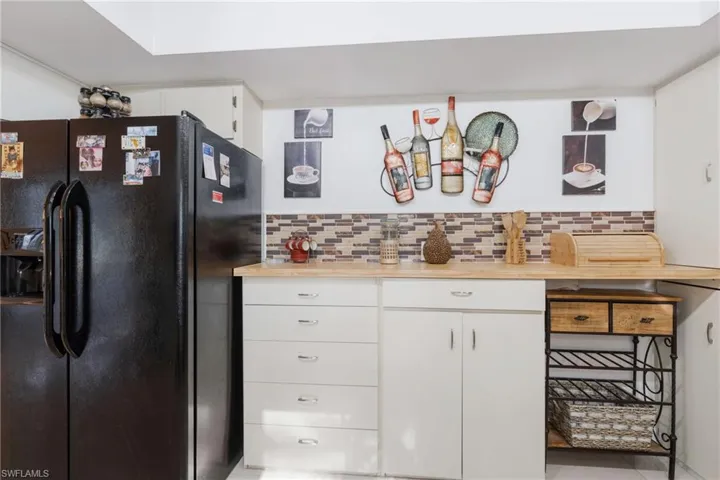 Kitchen with black fridge, light tile patterned floors, white cabinets, and backsplash