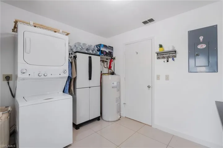 Laundry room with electric water heater, stacked washer / dryer, light tile patterned floors, and electric panel