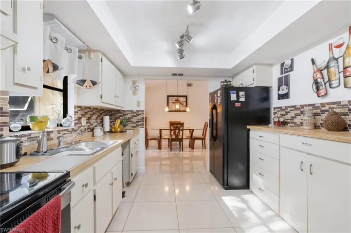 Kitchen with black fridge, decorative backsplash, white cabinets, and track lighting
