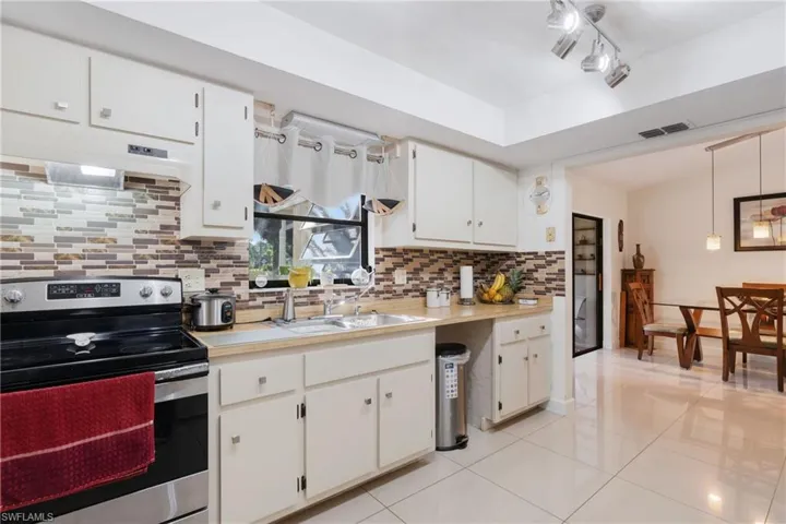 Kitchen featuring sink, stainless steel electric stove, decorative backsplash, white cabinetry, and custom range hood