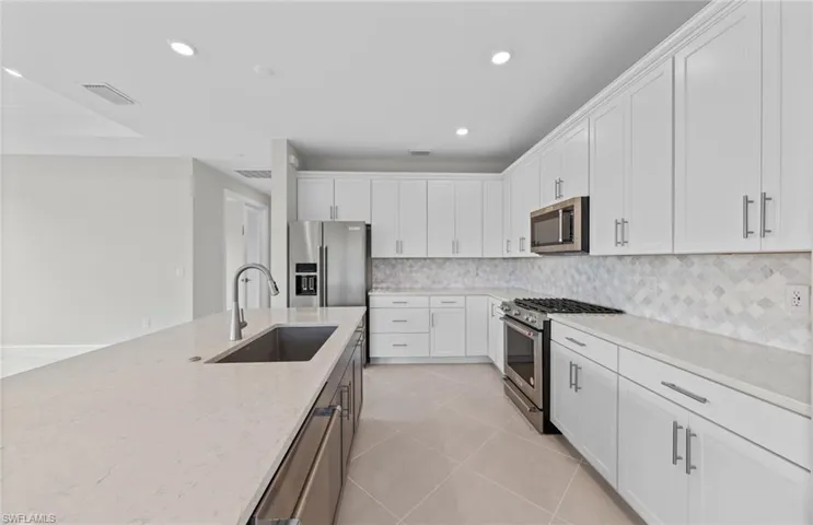 Kitchen featuring appliances with stainless steel finishes, white cabinetry, sink, and tasteful backsplash