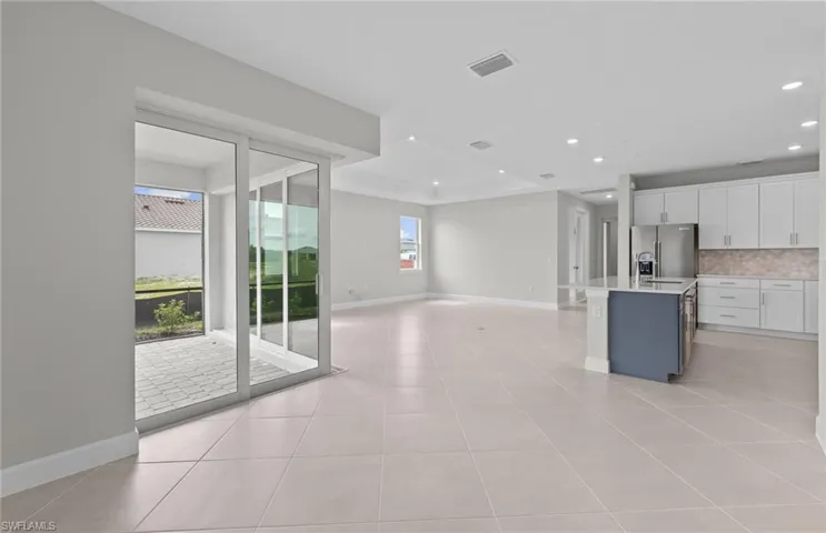 Kitchen with an island with sink, white cabinets, a healthy amount of sunlight, and stainless steel fridge