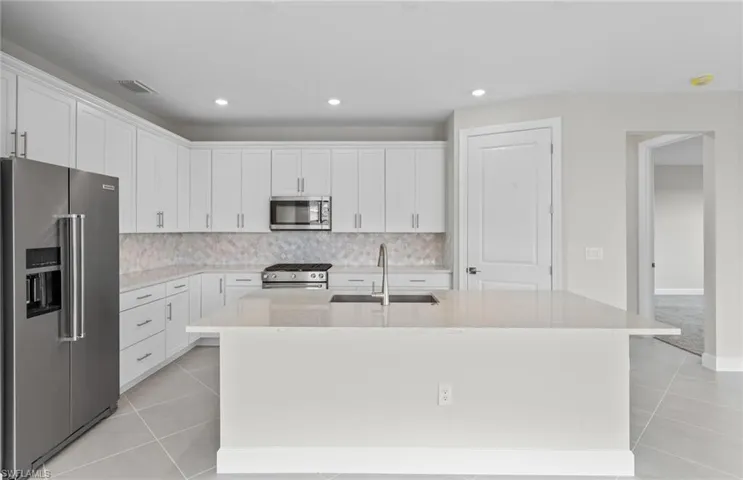 Kitchen featuring white cabinets, light tile patterned floors, stainless steel appliances, a kitchen island with sink, and sink