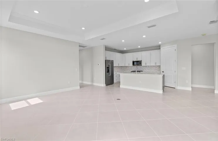 Kitchen featuring a kitchen island with sink, backsplash, white cabinetry, appliances with stainless steel finishes, and a tray ceiling