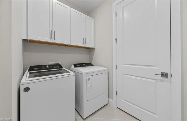 Clothes washing area with cabinets, light tile patterned flooring, and washing machine and dryer