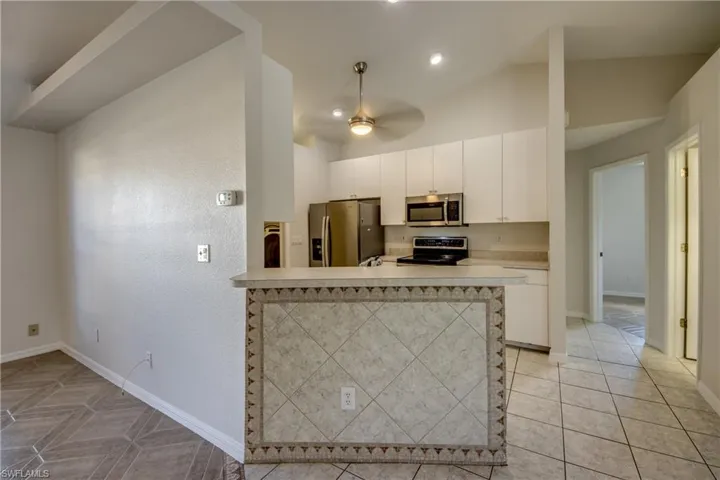 Kitchen featuring stainless steel appliances, vaulted ceiling, light countertops, white cabinets, and a peninsula