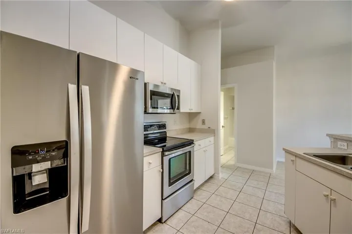 Kitchen with stainless steel appliances, light countertops, white cabinets, and light tile patterned floors