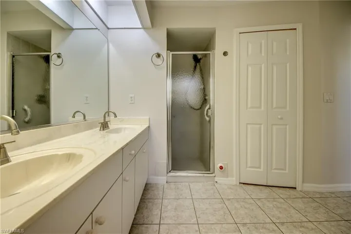 Full bath with a closet, double vanity, a stall shower, and light tile patterned flooring
