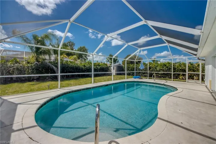 Outdoor pool featuring a sunroom, glass enclosure, a patio, a shed, and a lawn