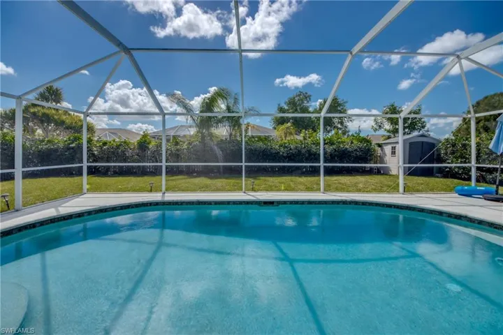 Outdoor pool with a sunroom, glass enclosure, a storage unit, and a yard