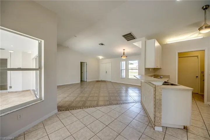 Kitchen featuring light countertops, decorative light fixtures, a peninsula, white cabinetry, and light tile patterned flooring