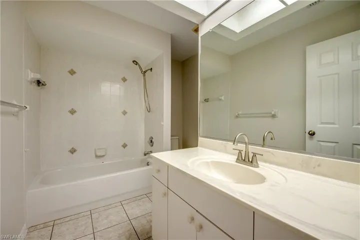 Bathroom with vanity, light tile patterned floors, tub / shower combination, and a skylight