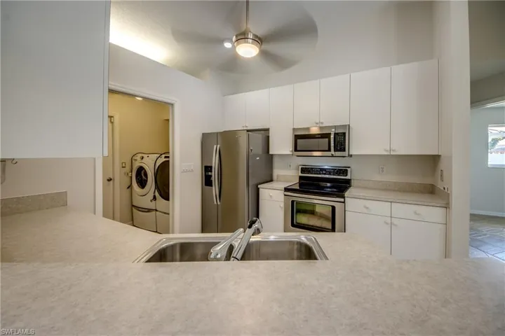 Kitchen featuring stainless steel appliances, white cabinetry, light countertops, ceiling fan, and separate washer and dryer