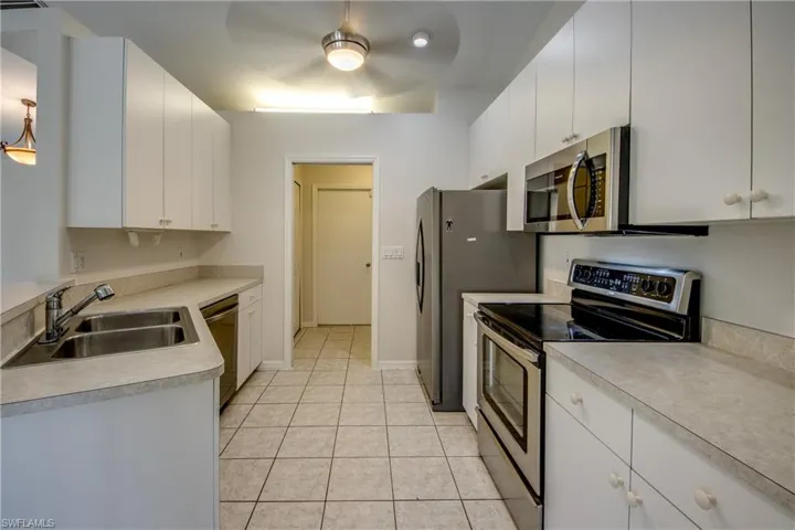 Kitchen with stainless steel appliances, light countertops, white cabinets, ceiling fan, and light tile patterned floors