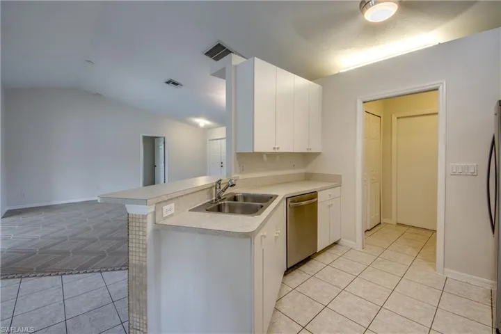 Kitchen featuring light countertops, white cabinets, stainless steel appliances, light tile patterned floors, and vaulted ceiling