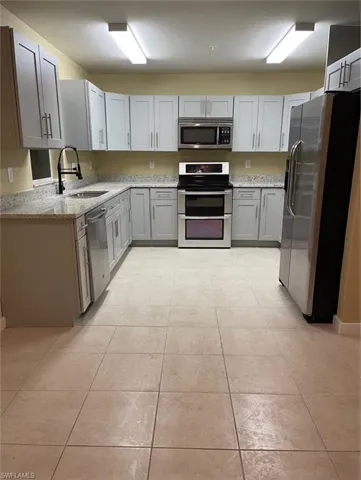 Kitchen featuring stainless steel appliances, light stone counters, gray cabinetry, and light tile patterned floors