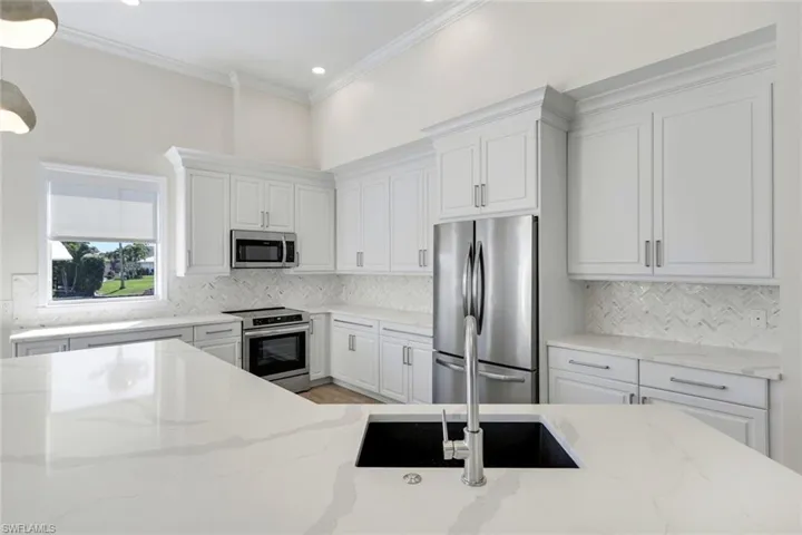 Kitchen featuring stainless steel appliances, white cabinetry, light stone countertops, pendant lighting, and ornamental molding
