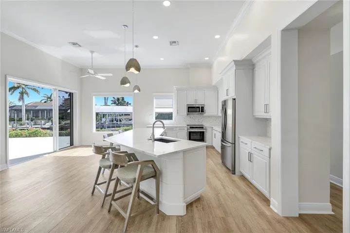 Kitchen featuring white cabinetry, a breakfast bar, a kitchen island with sink, hanging light fixtures, and stainless steel appliances