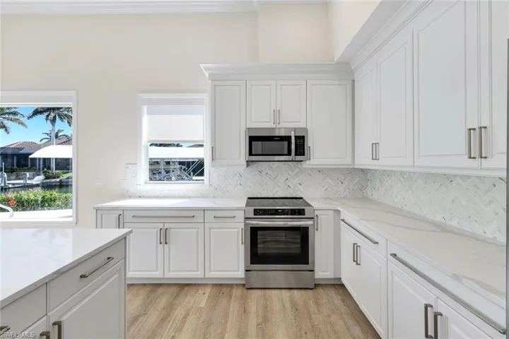 Kitchen featuring stainless steel appliances, white cabinetry, light wood-style floors, light stone counters, and tasteful backsplash