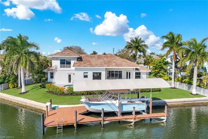 Rear view of house with boat lift, a water view, and stucco siding