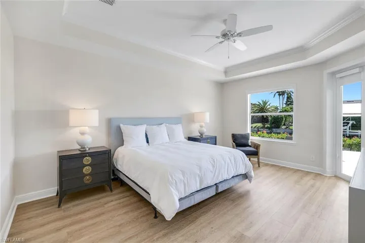 Primary Bedroom with light wood-type flooring, access to outside, crown molding, a raised ceiling, and ceiling fan