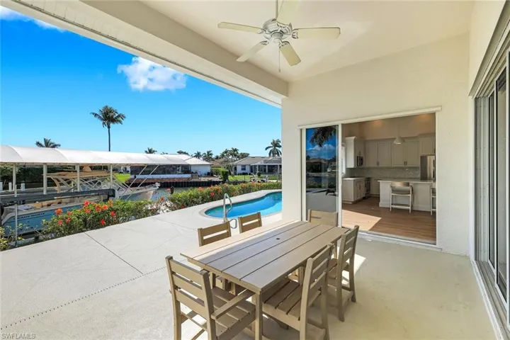 View of patio with outdoor dining area, a ceiling fan, an outdoor pool, and a boat dock